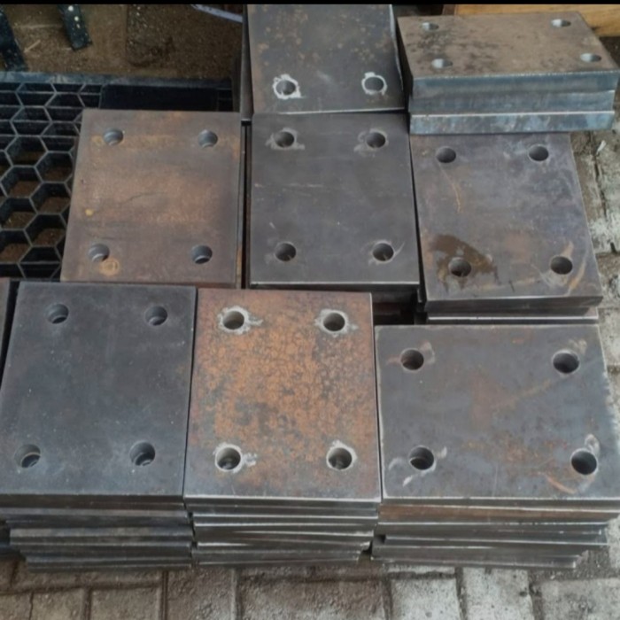 A stack of raw rectangular iron base plates with pre-drilled holes kept in a workshop for checking thickness and dimensions.